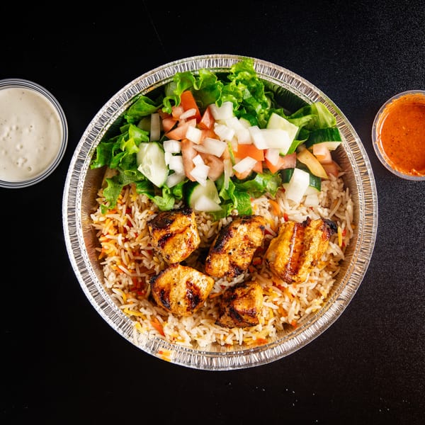 Grilled chicken skewers, rice, and a fresh salad in a foil container with sauces on the side.