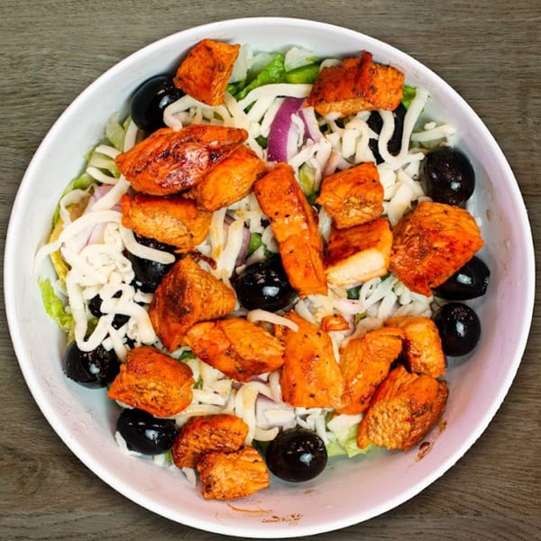 A Mediterranean salad with grilled chicken, black olives, shredded cheese, and red onion.